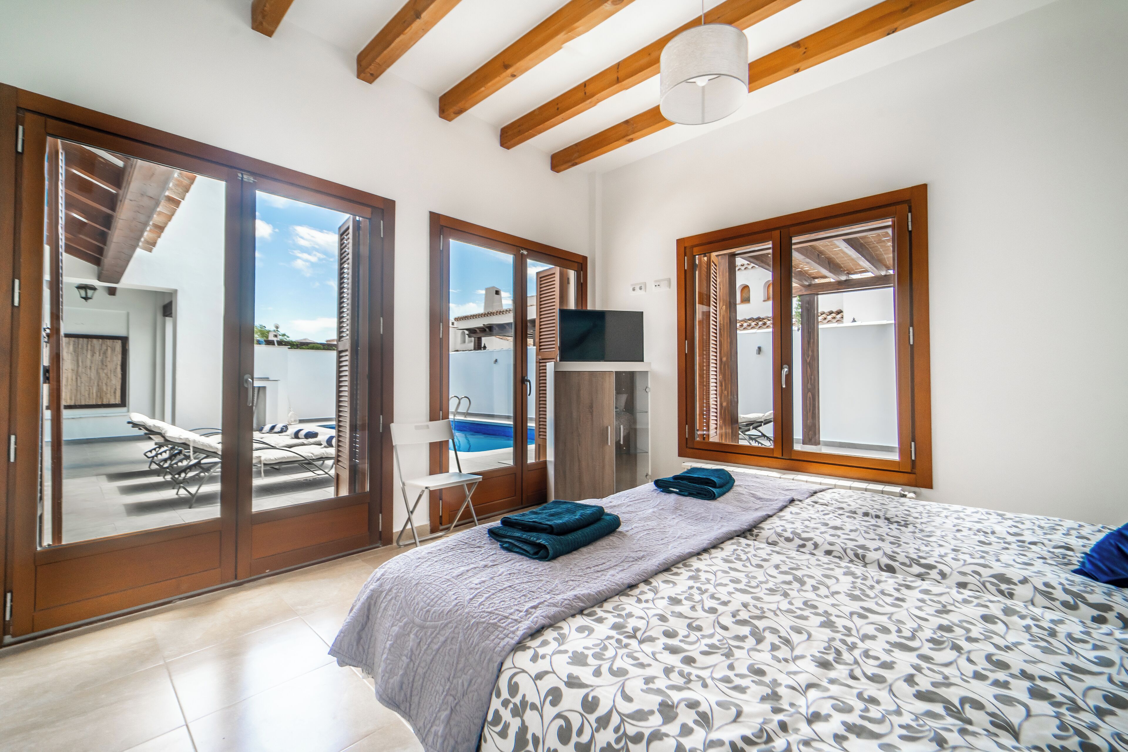 A bedroom with a bed, a TV, and a view of a pool and outdoor seating area.