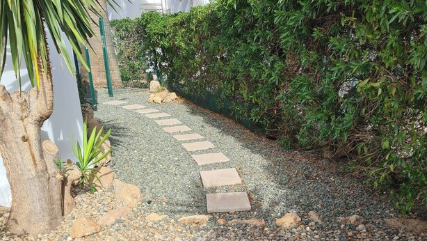 A gravel path with stepping stones leading through a garden area with a palm tree and dense foliage. - Sunset Villa not for Rent (Pulpi)