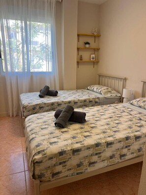 A room with two beds, a window with curtains, a shelf with decorative items, and a lamp. - 2-bed Apartament Rosaleda Monterey (Denia)