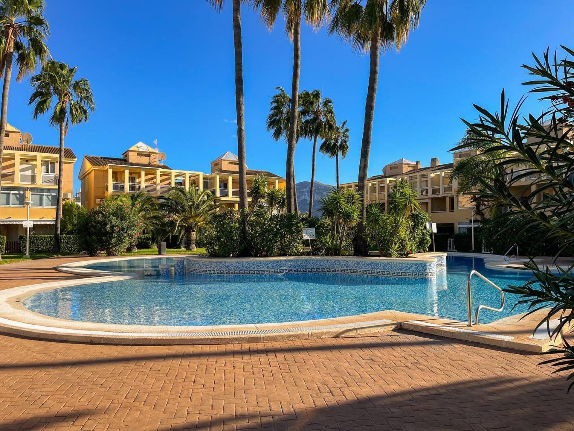 A swimming pool surrounded by palm trees and buildings with a clear blue sky.