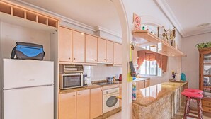 A kitchen with wooden cabinets, a microwave, a washing machine, and a sink. There is a bar stool and a bottle of hand sanitizer on the counter. - 2bed Apartment - Sleeps 5 - Pool, Parking, Pets (Benferri)