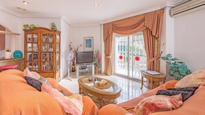 A living room with a sofa set, a wooden cabinet, a television, and a fan. - 2bed Apartment - Sleeps 5 - Pool, Parking, Pets (Benferri)