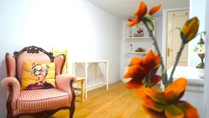 Une pièce comprenant un fauteuil à revêtement rose, une table d’appoint blanche et une étagère blanche ornée d’objets décoratifs.