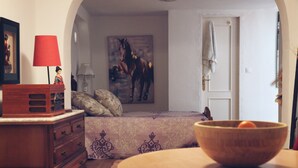 Une chambre à coucher avec un lit, une commode en bois, une lampe rouge, un tableau et un bol en bois posé sur une table.