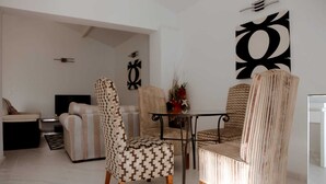 Un salon moderne comprenant un canapé, deux fauteuils à motifs, une table basse et une table à manger avec des chaises.