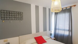 Habitación de hotel con cama, lámpara de pared, ventana con cortinas y una mesita con lámpara.
