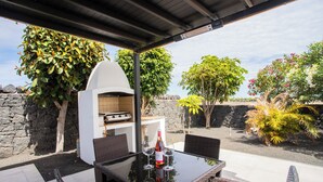 An outdoor patio with a glass table, wicker chairs, a barbecue grill, and various plants. - Gorgeous Newly Renovated 4-bedroom Villa! (Yaiza)
