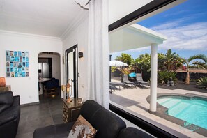 A modern living room with a pool view, featuring a black sofa, a dining area, and a wall with framed pictures. - Gorgeous Newly Renovated 4-bedroom Villa! (Yaiza)