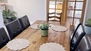 A dining area with a wooden table, black leather chairs, and two potted plants.
