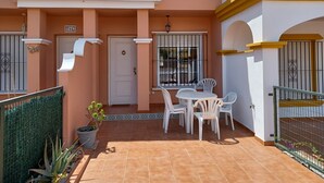 Un bâtiment à deux étages doté d’un patio comprenant une table et des chaises, une porte et une fenêtre avec des barreaux.