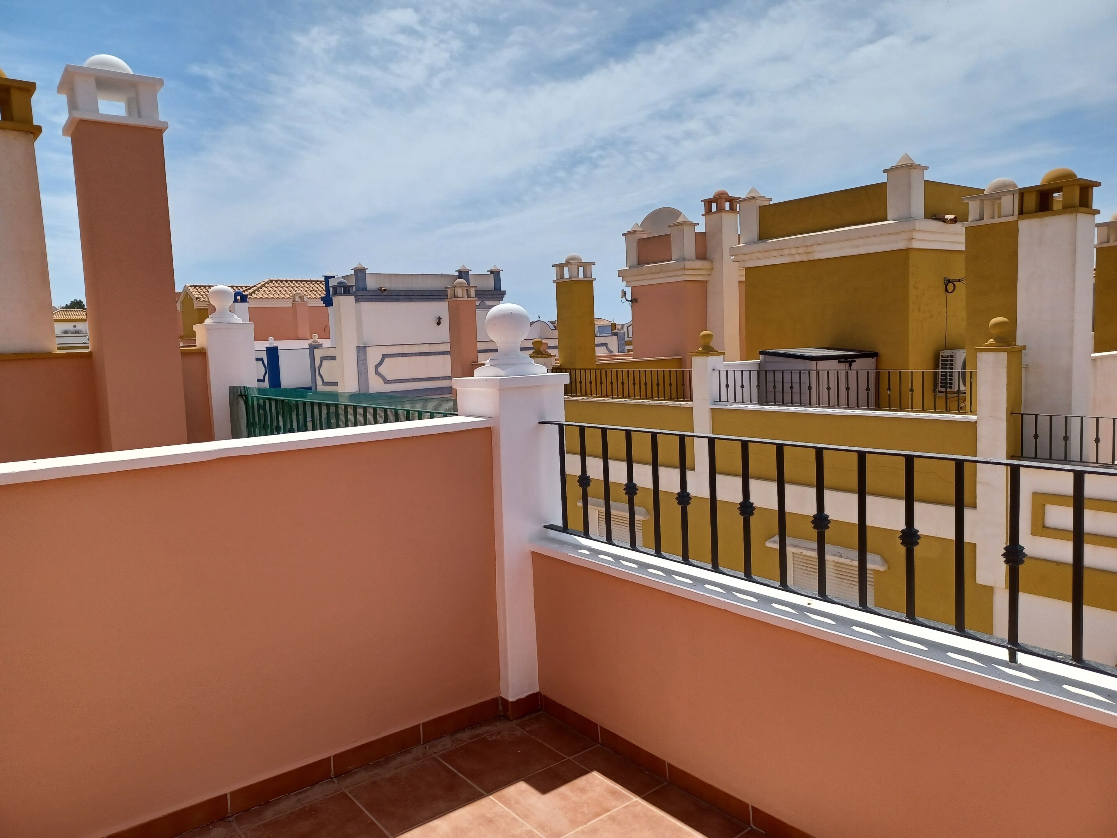 A balcony with a tiled floor, white balustrade, and a view of neighboring buildings.