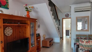 Un salon avec un meuble en bois, une télévision et un escalier menant à une autre pièce.