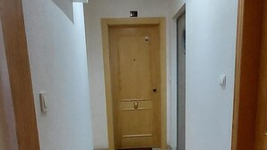 Egy folyosó, a végén egy faajtóval, csempézett padlóval és egy mennyezeti lámpatesttel.