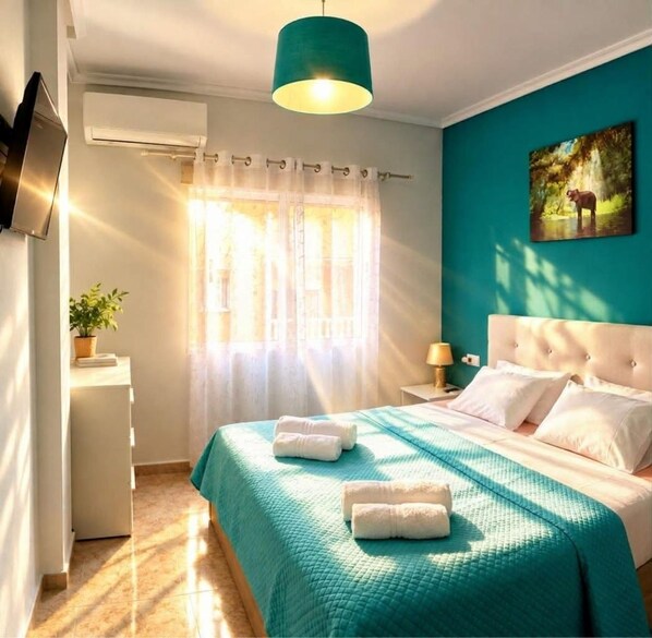 A hotel room with a bed, a bedside table, a lamp, a painting, and a window with curtains.