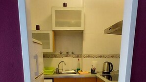 Egy keskeny konyha, fehér szekrényekkel, mikrohullámú sütővel, vízforralóval és mosogatóval.