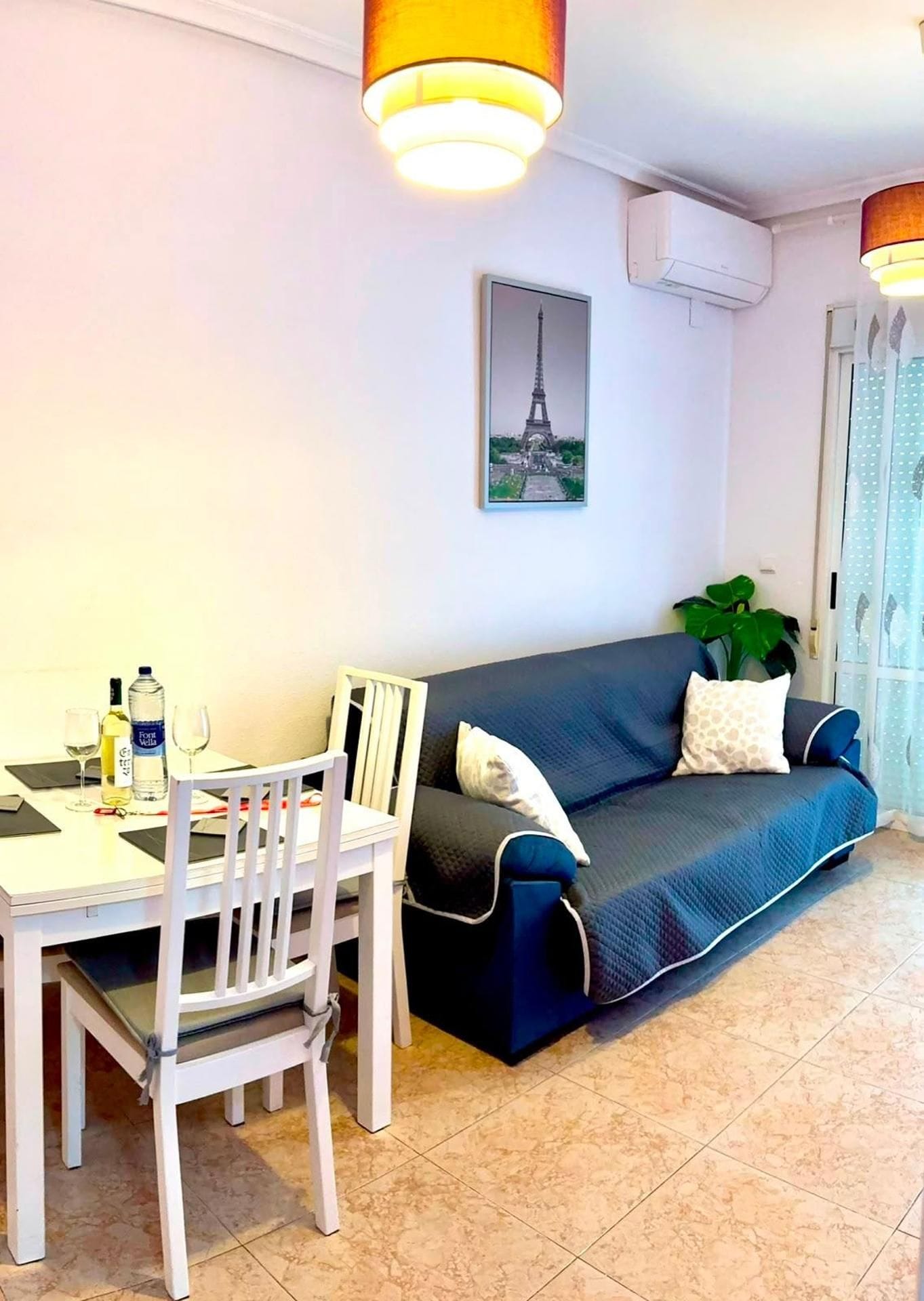 A living room with a dining table, chairs, a sofa, and a potted plant.