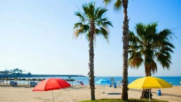 Platja de sorra amb palmeres i parasols de platja.