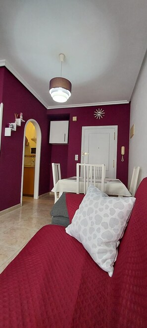 A room with a red carpet, a bed with a white and grey patterned pillow, a white chair, a small table, and a white door. - Ellite Xiii Apartment Playa Naufragos Torrevieja! (Torrevieja)