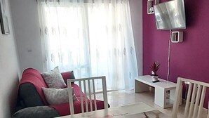 Egy étkező, melyben fehér asztal és székek találhatók, a falak lila színűek, és a falra van szerelve egy televízió.