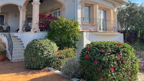 Una casa de dos plantas con un porche cubierto, un balcón y un muro de piedra.