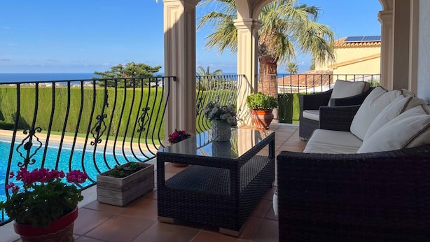 Un balcón con vista a la piscina, mobiliario exterior y cielo despejado.