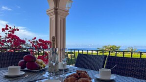 Una mesa dispuesta con una botella de Moët champagne, copas, un plato de croissants y una taza de café, con vistas a un paisaje pintoresco.