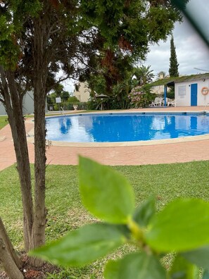 A swimming pool with a tiled deck, surrounded by grass and trees. - Beautiful 4 Bedroom Duplex Apartment (Estepona)