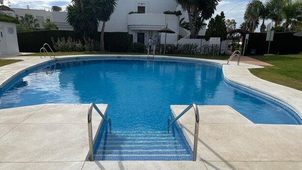 A swimming pool with a clear blue water, surrounded by a concrete deck and a small set of stairs leading into the pool. - Beautiful 4 Bedroom Duplex Apartment (Estepona)