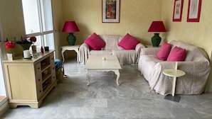 A living room with a beige sofa, a white coffee table, and a beige cabinet. There are two lamps on side tables, and a framed picture on the wall. - Beautiful 4 Bedroom Duplex Apartment (Estepona)
