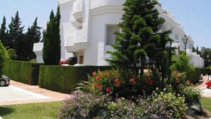 A modern white building with a curved facade, surrounded by well-maintained gardens and a clear sky. - Beautiful 4 Bedroom Duplex Apartment (Estepona)