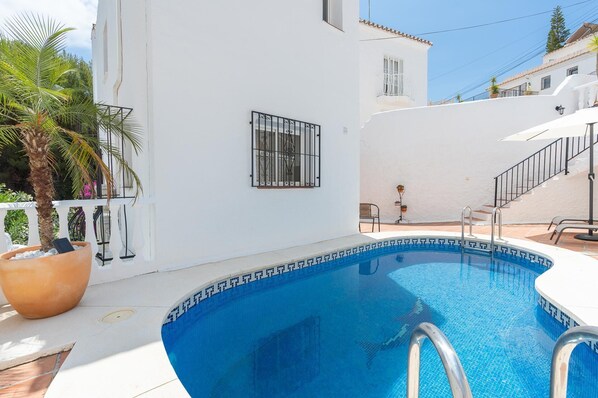 Una piscina con bordo piastrellato, un muro bianco con una finestra e una scala che conduce a un balcone.