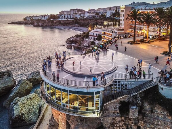 Une promenade en bord de mer agrémentée d’une plateforme circulaire offrant une vue panoramique, d’un restaurant avec terrasse et d’un hôtel doté de balcons avec vue sur la mer.