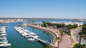 A marina with numerous boats docked, a pedestrian walkway, and a view of the sea and distant buildings. - Comfortable 2 Bed Apartment in Isla Canela Beach (Ayamonte)