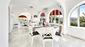 A spacious dining area with white tables and chairs, arched ceilings, and large windows offering views of the landscape. - Most Luxurious Villa on the Costa del Sol (Mijas)
