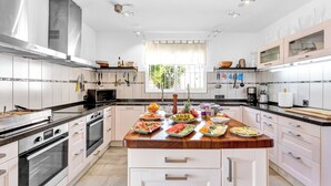 A modern kitchen with white cabinetry, stainless steel appliances, and a central island with various food items. - Most Luxurious Villa on the Costa del Sol (Mijas)
