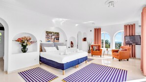 A modern hotel room with a large bed, a TV, a seating area with a table, and a view of the outdoors. - Most Luxurious Villa on the Costa del Sol (Mijas)