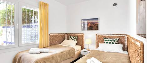 Habitación de hotel con dos camas, una ventana con cortinas, una mesita con lámpara y un cuadro en la pared.