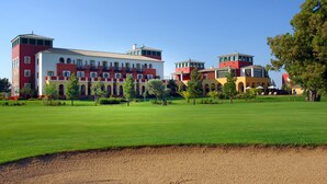 Un grand immeuble à étages, doté d’une façade rouge et blanche, entouré d’une pelouse bien entretenue et d’arbres.