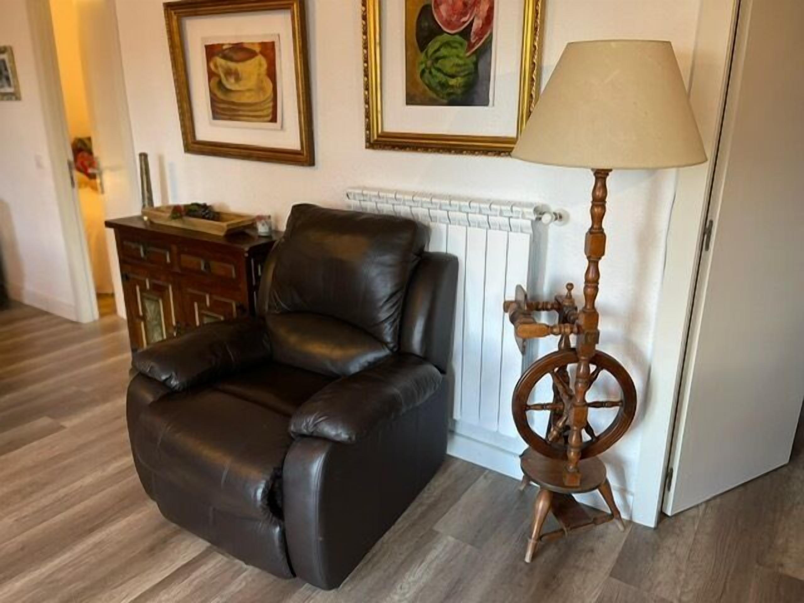 Una habitación con una butaca de cuero negro, suelo de madera, un radiador y una lámpara con base de madera.