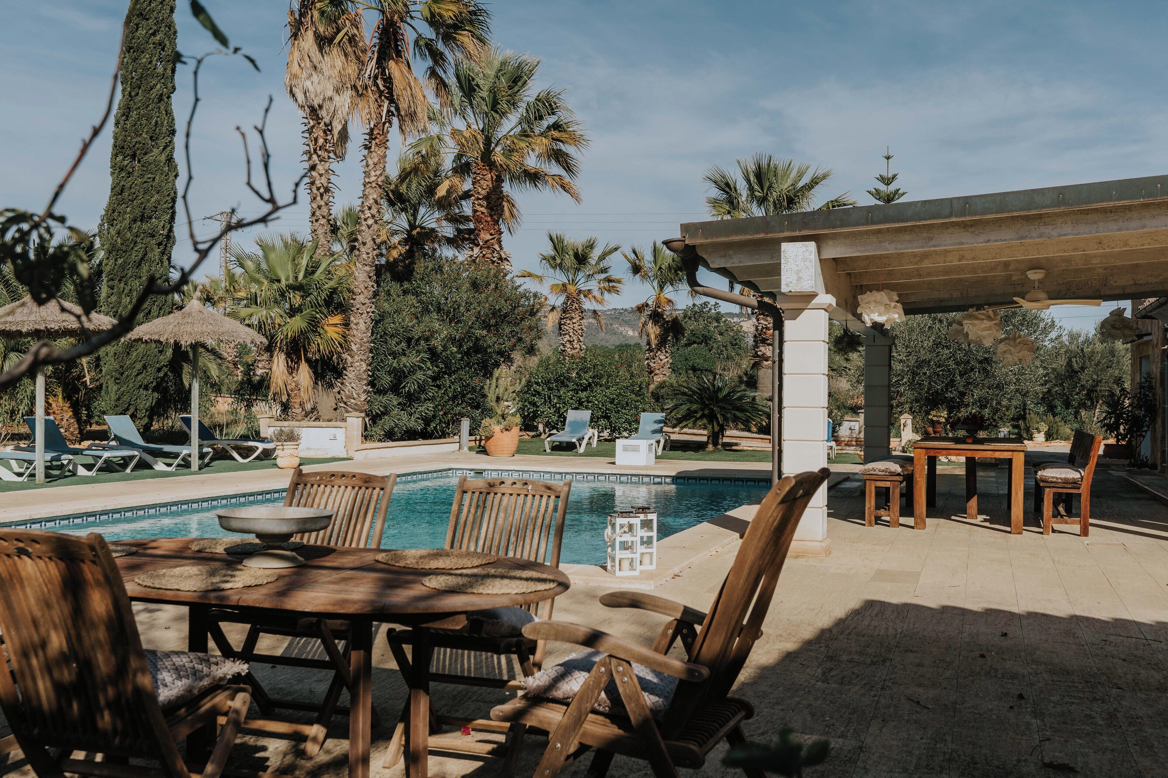 A poolside area with a wooden table and chairs, lounge chairs, and a pergola.