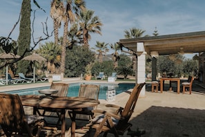 A poolside area with a wooden table and chairs, lounge chairs, and a pergola.