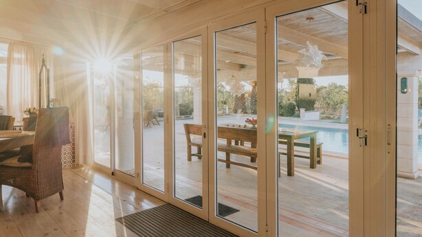Ein geräumiges Zimmer mit großen Schiebeglastüren, die auf eine Außenpatio-Terrasse mit Pool, Holzmöbeln und einer Pergola führen.