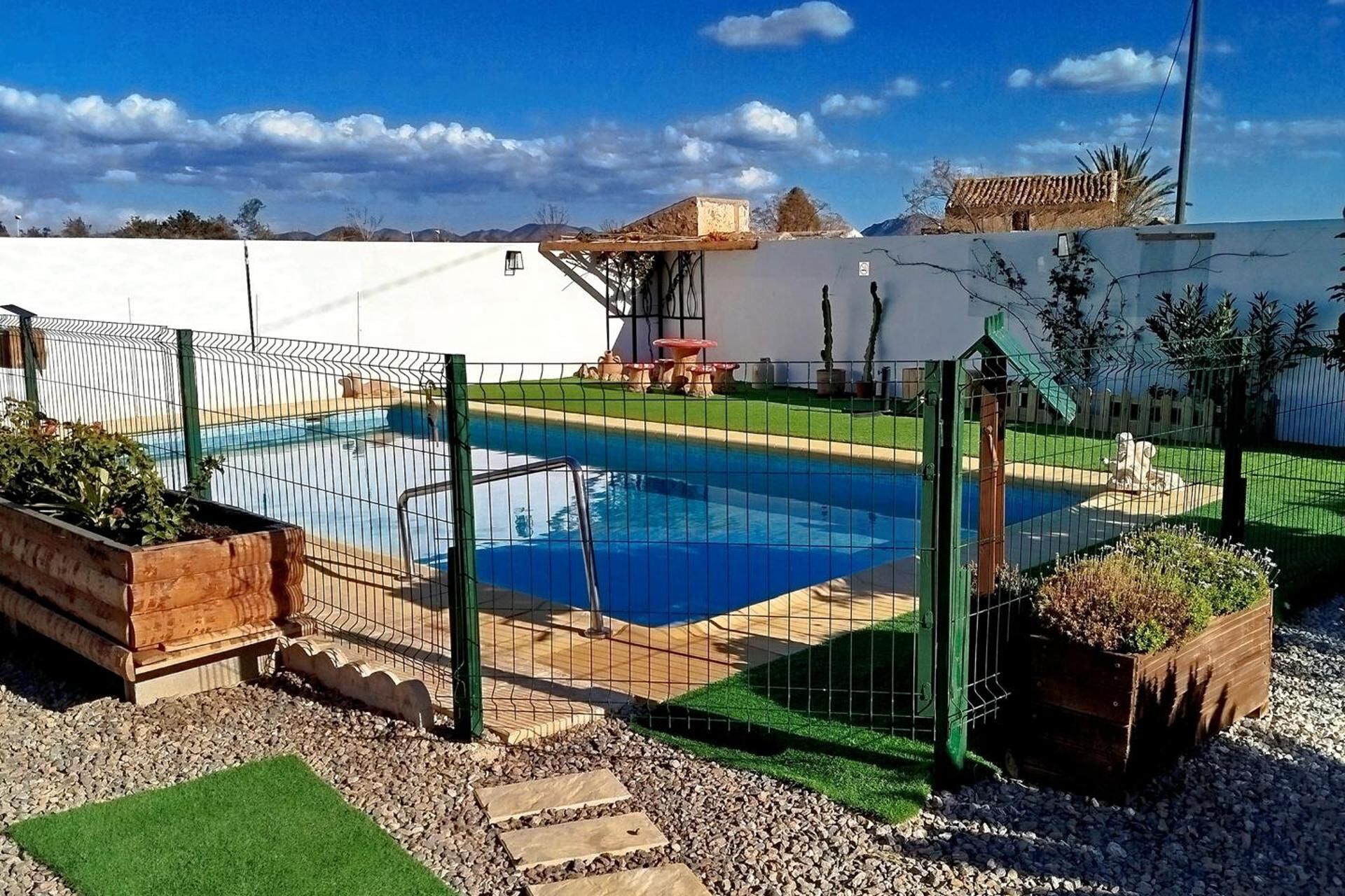 A swimming pool surrounded by a fence, with a grassy area and a few potted plants.