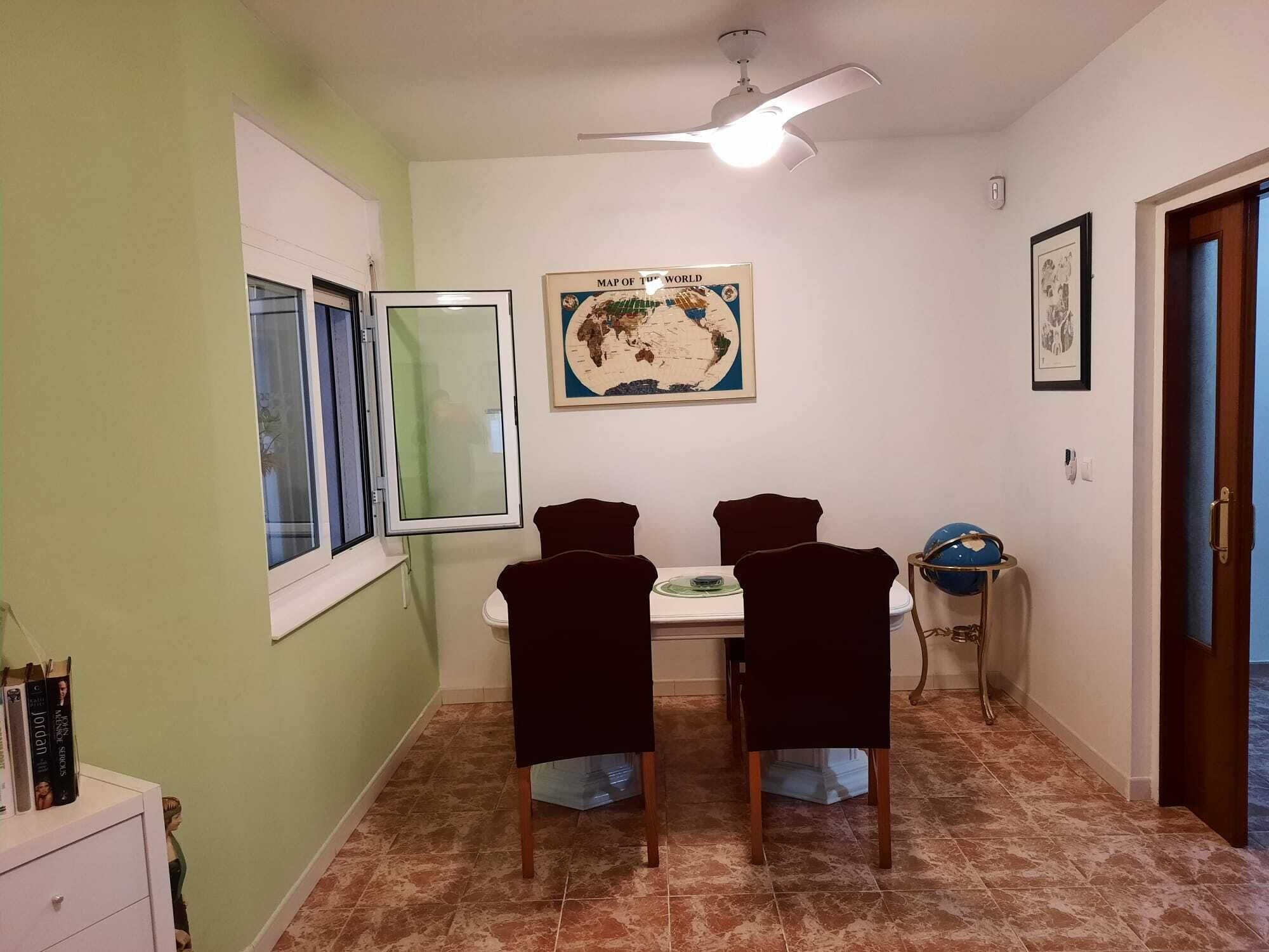 Un comedor con una mesa y cuatro sillas, un globo en un atril, un ventilador de techo y un mapa del mundo en la pared.