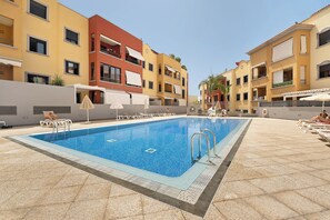 A swimming pool with lounge chairs and umbrellas, surrounded by multi-story buildings with balconies and outdoor seating. - Bonito Apto Montenerife Adeje (Adeje)