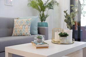 A modern living room with a grey sofa, patterned cushions, a white coffee table, a glass bowl with a plant, and a potted plant in a gold wire basket. - Bonito Apto Montenerife Adeje (Adeje)
