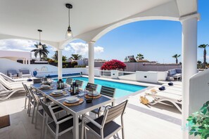 An outdoor pool area with a dining setup, lounge chairs, and a view of the surrounding landscape. - Remarkable 5-bed Villa in Playa Blanca (Yaiza)