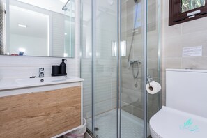 A modern bathroom with a glass shower enclosure, a white sink with a wooden cabinet, and a toilet. - Remarkable 5-bed Villa in Playa Blanca (Yaiza)