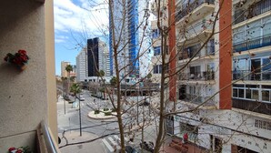 Une vue depuis un balcon donnant sur une rue de la ville, avec de hauts immeubles, un carrefour giratoire et des voitures garées.