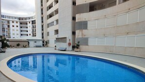 Une piscine dotée d’une plage carrelée, entourée d’un bâtiment comportant de nombreux balcons et présentant une conception architecturale aux lignes courbes.
